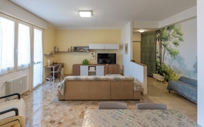 A compact living space with a kitchenette, a sofa, a television, and a mural. - HouSmart Giambologna 8 (Bologna)