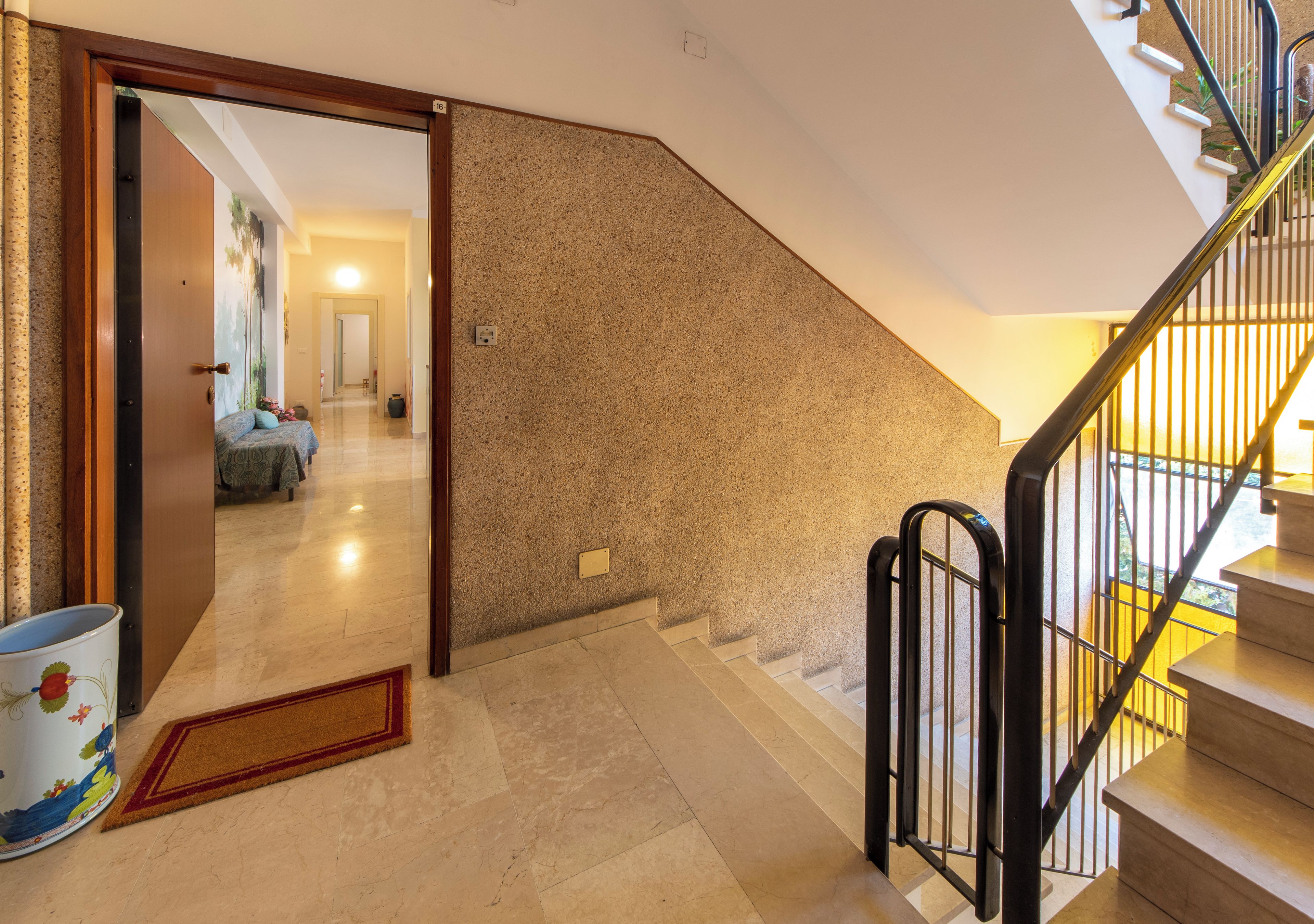 A hallway with a carpeted floor, a door leading to another room, and a staircase with a metal railing.