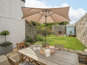 A wooden patio table with a beige umbrella, surrounded by potted plants and a stone wall. - Swn y Mor (Beaumaris)