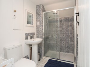 A bathroom with a white sink, a toilet, and a glass-enclosed shower area. - Swn y Mor (Beaumaris)