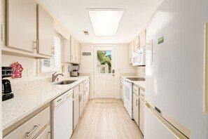 A modern kitchen with white cabinetry, a built-in oven, a microwave, and a coffee maker. - Beach House | Walk to Beach | Golf Carts OK (Myrtle Beach)