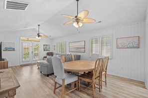 A dining area with a wooden table and chairs, a ceiling fan, and a painting on the wall. - Beach House | Walk to Beach | Golf Carts OK (Myrtle Beach)