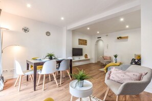 Un salon moderne comprenant un coin repas, un téléviseur à écran plat et un canapé agrémenté d’un plaid.