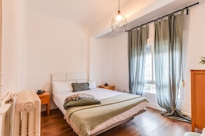 Ein Schlafzimmer mit einem Bett, einem Nachttisch, einem Heizkörper und einem Fenster mit Vorhängen.