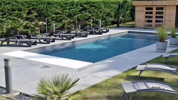 Une piscine rectangulaire, dotée de chaises longues et d’une petite structure en bois.