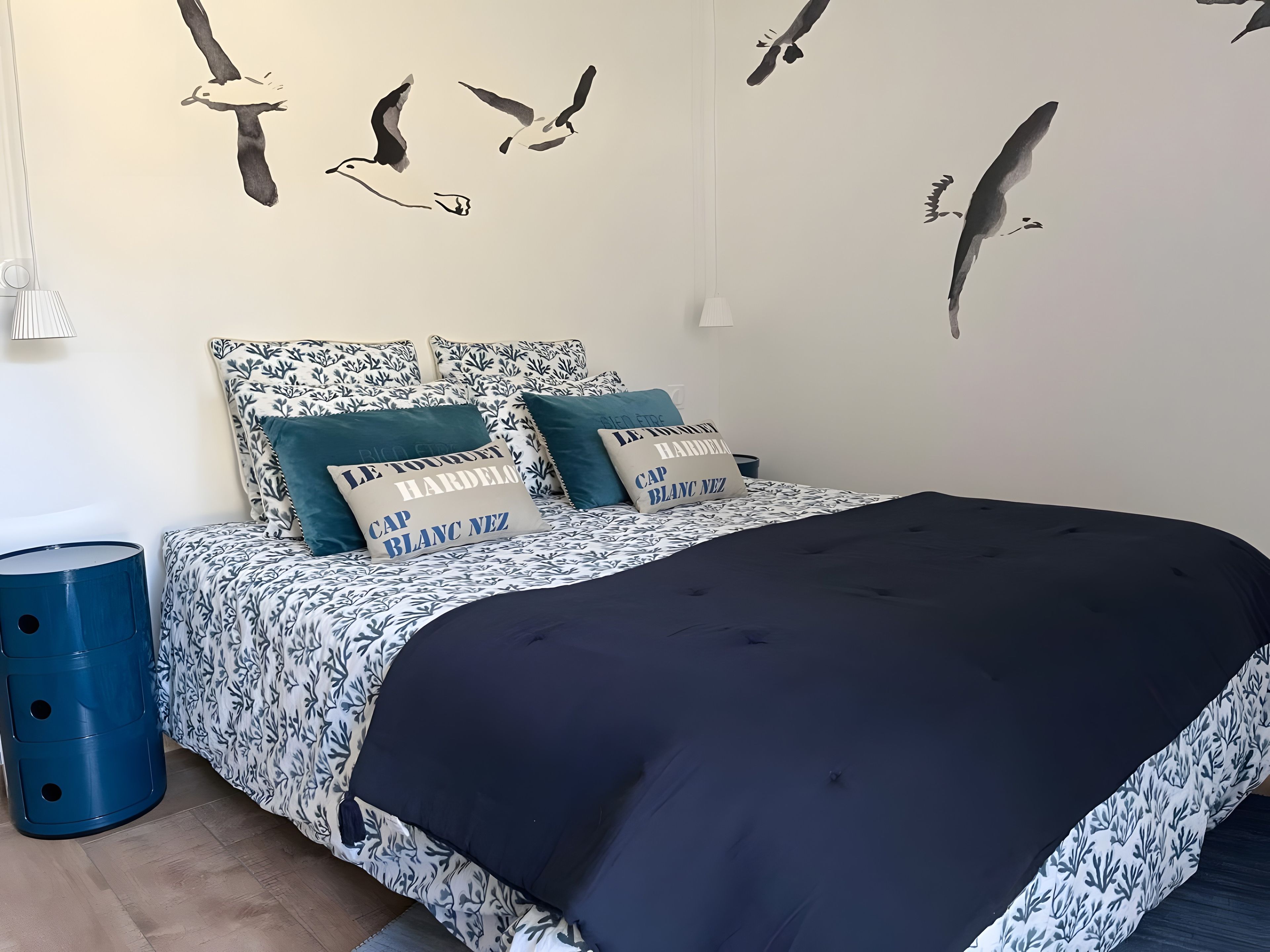 Une chambre à coucher avec un lit, des oreillers, une poubelle bleue et des autocollants décoratifs représentant des oiseaux sur les murs.