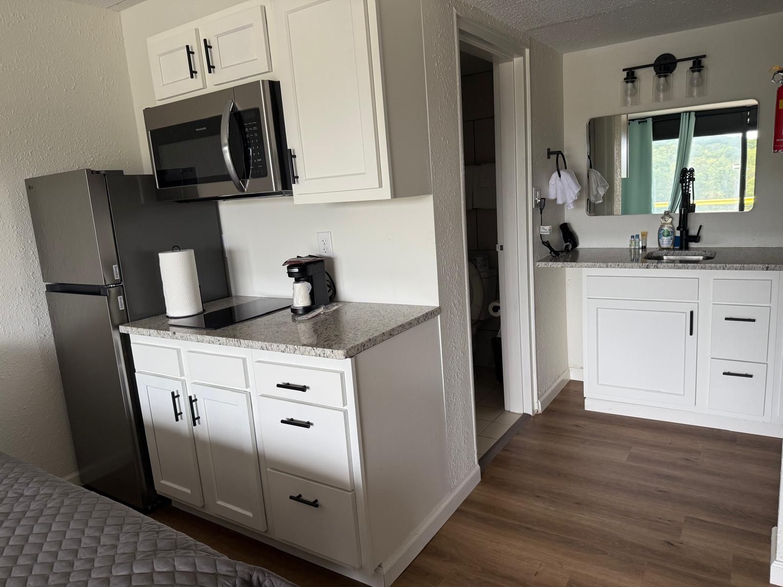 Una cocina moderna con armarios blancos, un refrigerador de acero inoxidable, un microondas y una cafetera.