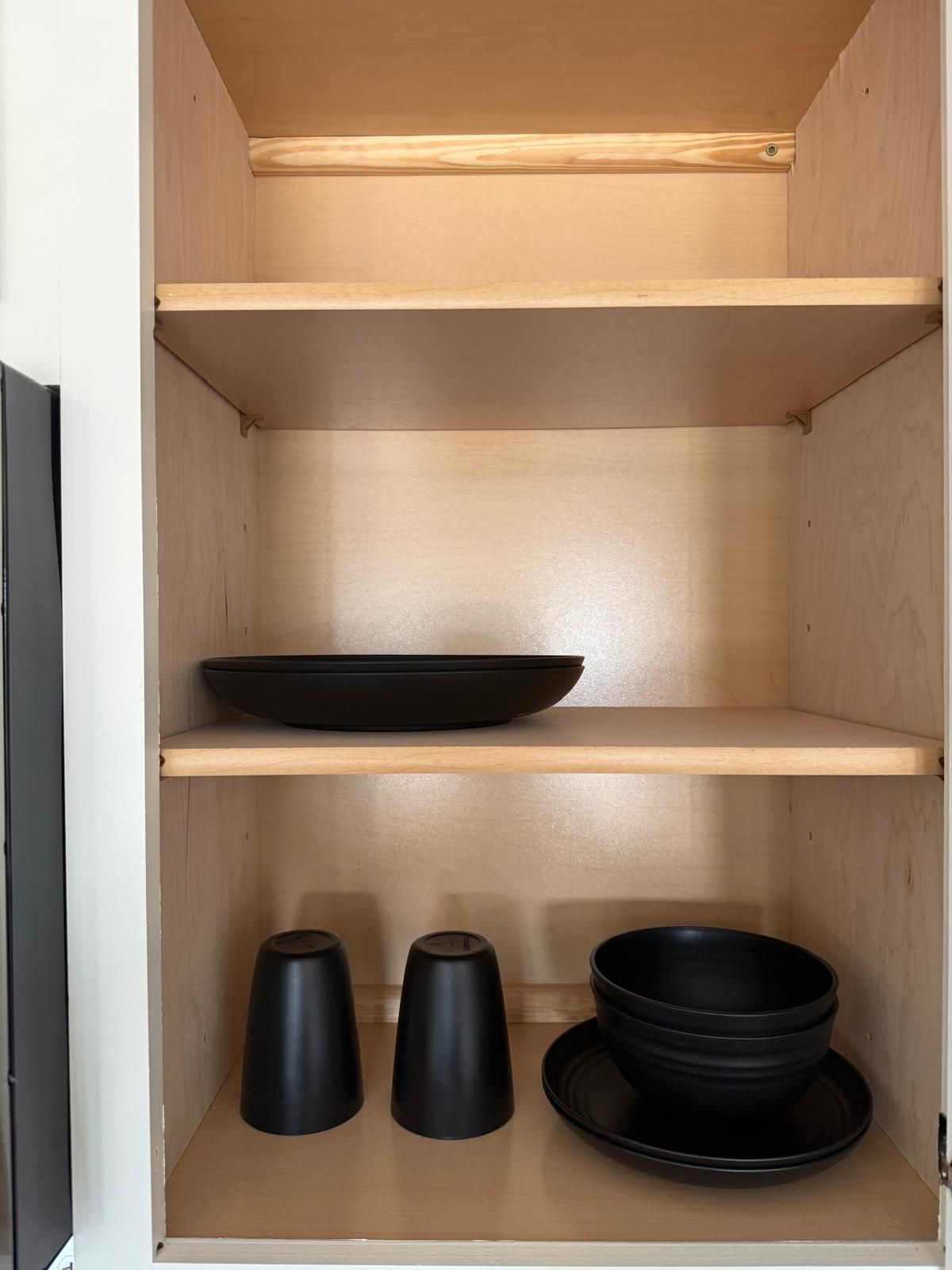 A wooden cabinet with three shelves, one of which holds a black bowl.