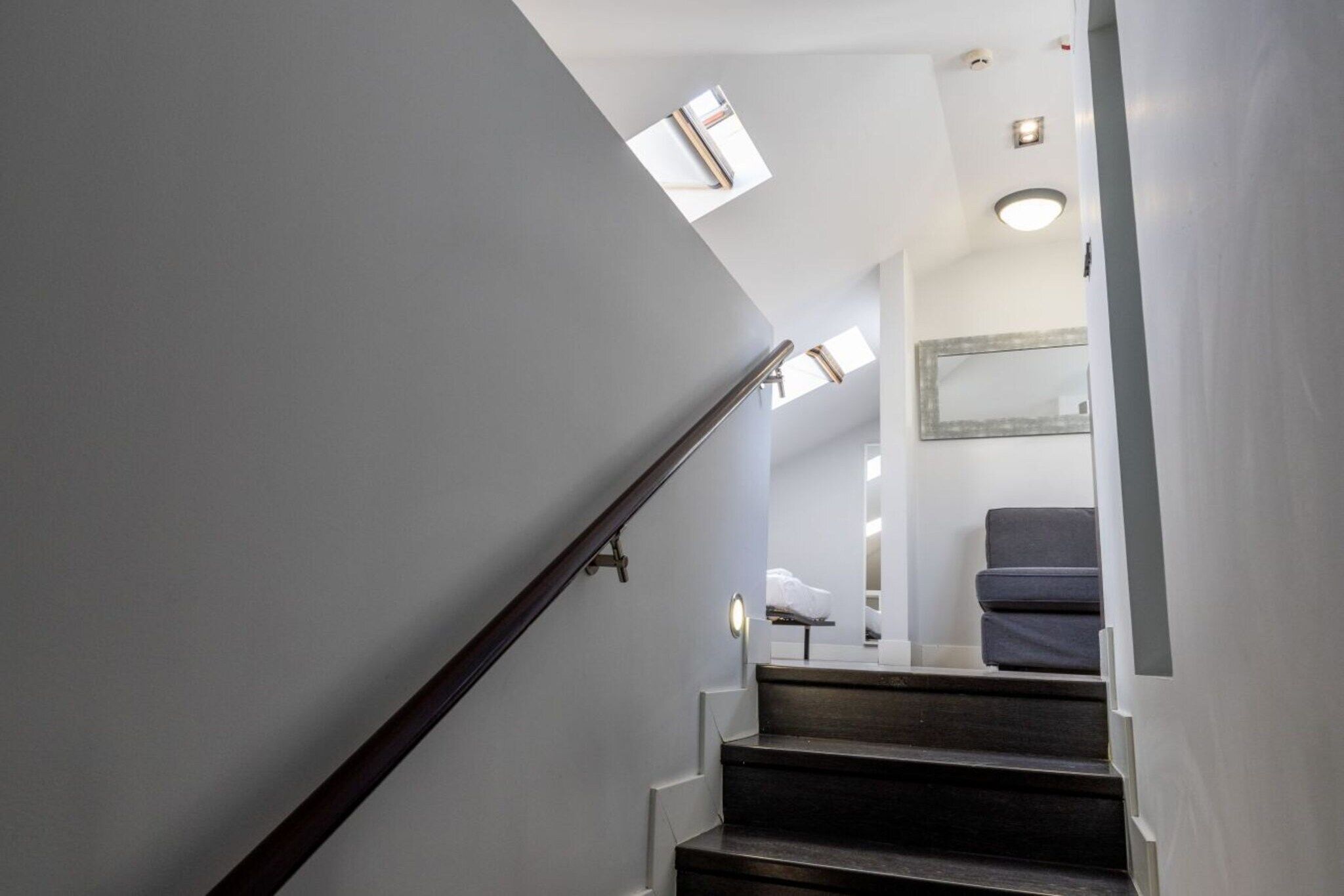 A staircase with a handrail leading to a landing where a bed and a chair are visible.