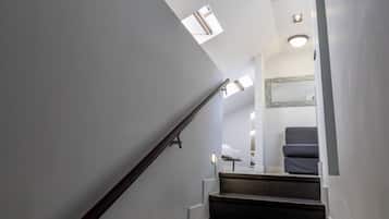 A staircase with a handrail leading to a landing where a bed and a chair are visible.