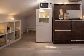 Een kleine keuken met een witte koelkast, een magnetron en een donker houten kast.