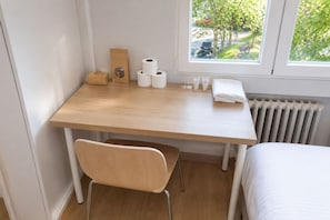 A small, neatly arranged bedroom with a wooden desk, a chair, a radiator, and a window with a view of trees and a street. - Bright room in Apartment, Chamartin (Madrid)