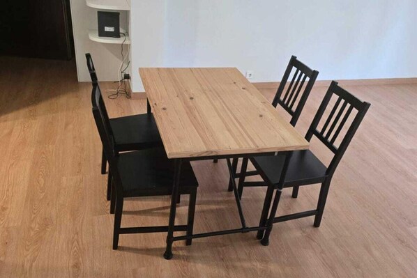Une table à manger en bois, quatre chaises noires, un mur blanc et un plancher en bois.