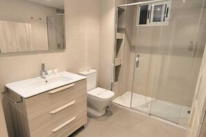 Une salle de bain moderne avec une douche à parois de verre, un lavabo blanc et des toilettes.