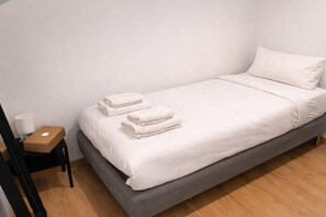 A single bed with white linens and pillows, a wooden nightstand with a box, and a white wall. - Private Stay with terrace, Madrid (Madrid)