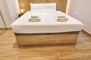 A neatly made bed with two folded towels on the headboard, a bedside lamp, and a wooden floor. - Modern Apartment near Las Ventas (Madrid)