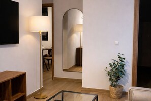 A room with a flat-screen TV, a floor lamp, a mirror, a wooden cabinet, a potted plant, and a small table. - Modern Apartment near Las Ventas (Madrid)