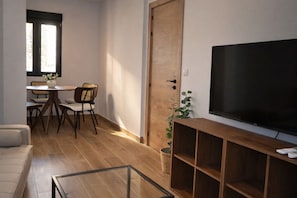 A living room with a flat-screen TV, wooden flooring, a sofa, a dining table with chairs, and a door. - Modern Apartment near Las Ventas (Madrid)