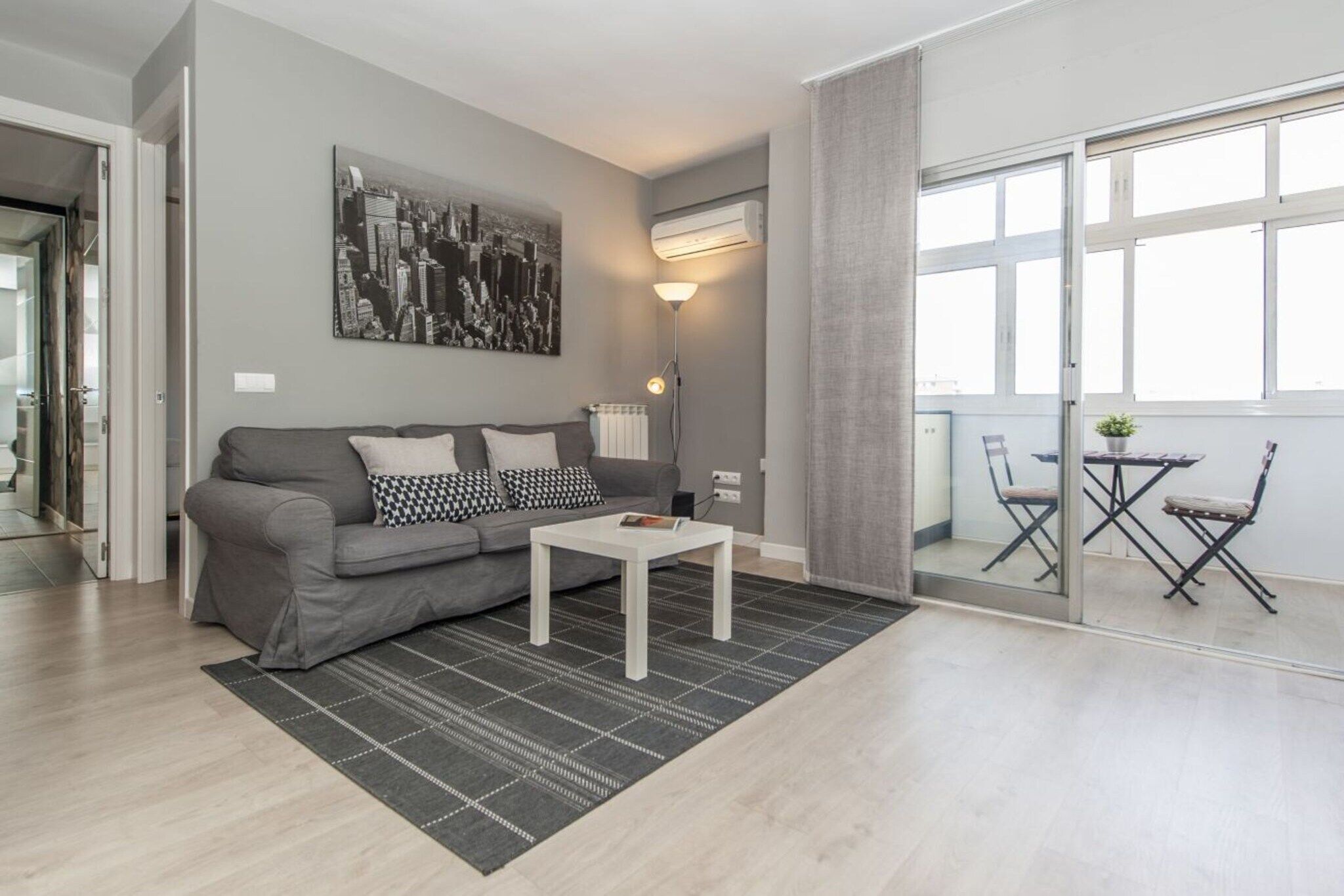 Un salon moderne avec un canapé gris, une table basse blanche et un tableau représentant un paysage urbain accroché au mur.