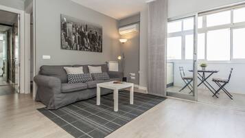 Un salon moderne avec un canapé gris, une table basse blanche et un tableau représentant un paysage urbain accroché au mur.