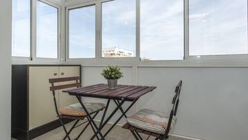 Une pièce avec une table et deux chaises, une plante en pot et une fenêtre donnant sur des immeubles.