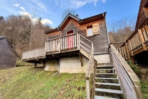 A wooden cabin with a balcony, a red door, and a staircase leading up to the entrance. - Family Chalet with Fireplace, Mont-Dore (Mont-Dore)