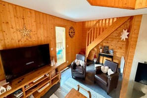 A wooden interior with a TV on a wooden stand, two leather armchairs, a wooden staircase, and a star decoration on the wall. - Family Chalet with Fireplace, Mont-Dore (Mont-Dore)