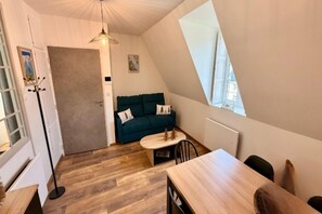 A compact living space with a loft-style ceiling, a sofa, a small table, and a dining area. - Mont-Dore Apartment, Mountain View (Mont-Dore)