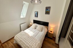 A bedroom with a bed, bedside tables, a window, and wall-mounted pictures. - Mont-Dore Apartment, Mountain View (Mont-Dore)