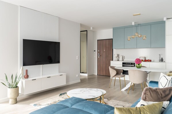 A modern living room with a flat-screen TV, a sofa, and a dining area with chairs. - Premium Apartments with Parking (Gdańsk)