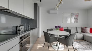 Une cuisine moderne dotée d’un four encastré, un coin repas avec une table ronde et des chaises, et un espace de détente avec un canapé et des coussins.