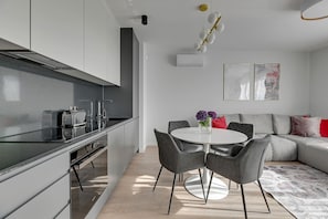 A modern kitchen with a built-in oven, a dining area with a round table and chairs, and a living area with a sofa and cushions. - Premium Apartments with Parking (Gdańsk)