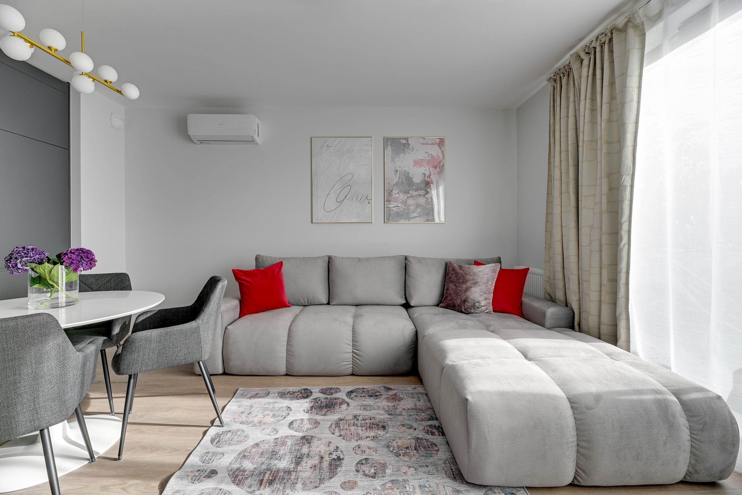 A modern living room with a grey sectional sofa, a round dining table, and a vase with flowers.