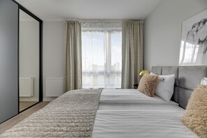 A modern bedroom with a large bed, a mirror, and a city view through the window. - Premium Apartments with Parking (Gdańsk)