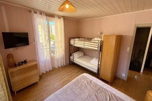 A bedroom with bunk beds, a television, a wooden dresser, and a door leading to another room. - Mont-Dore Apartment for 8 Guests (Mont-Dore)