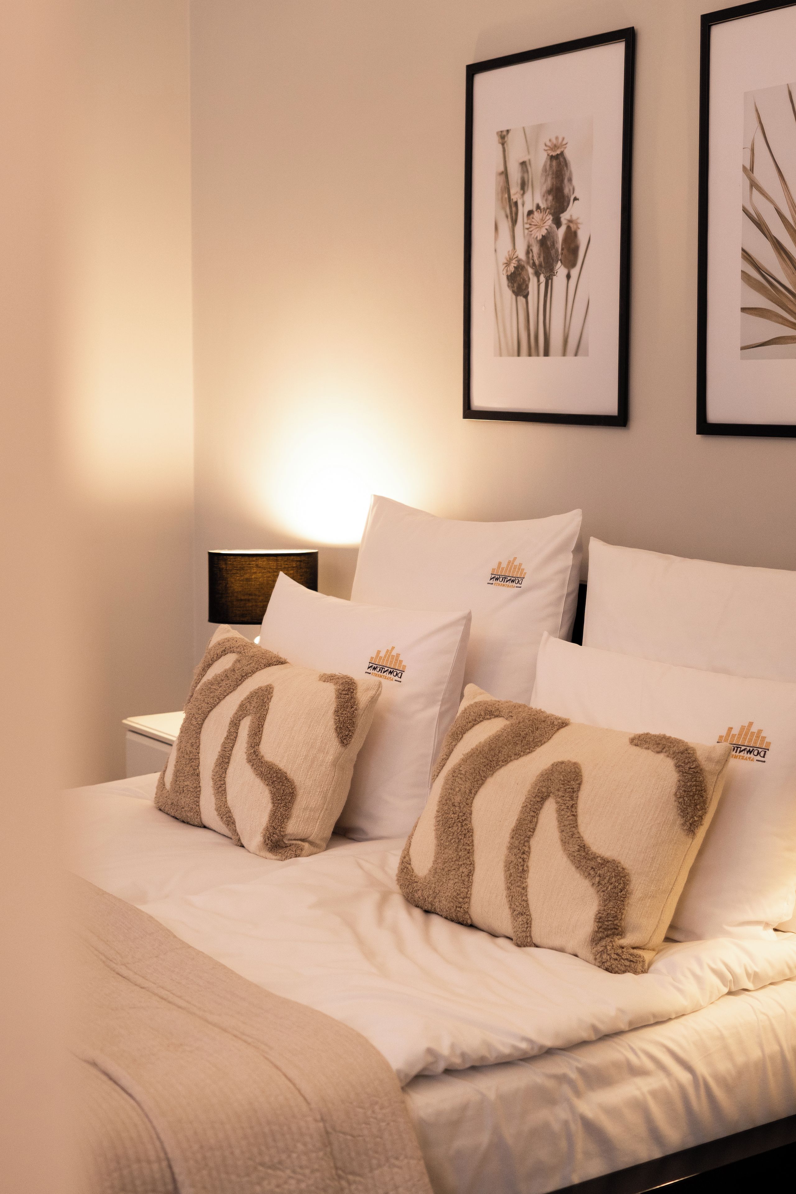 A neatly made bed with white bedding and two decorative pillows with a brown pattern.