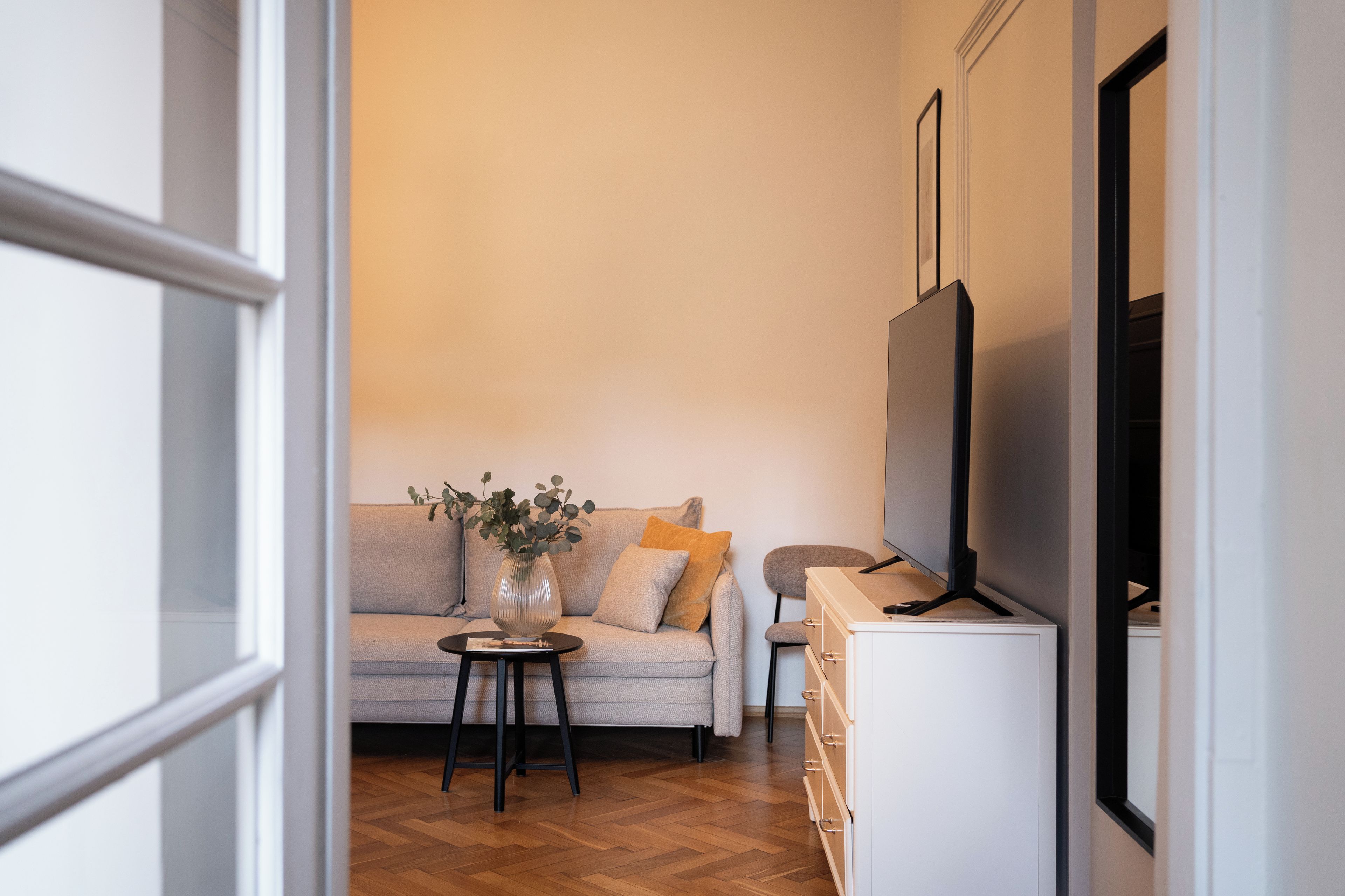 Una sala de estar con un sofá, una mesita con un florero y un mueble para televisión.
