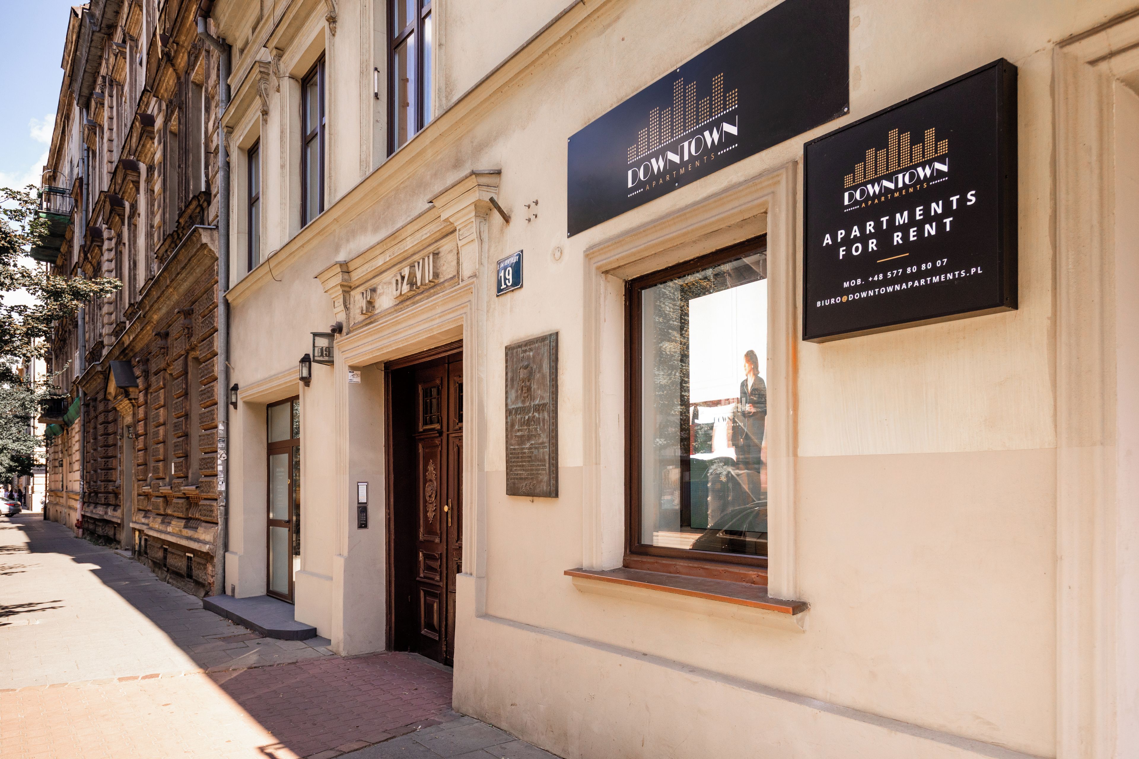 A building with a sign for 'Downtown Apartments for Rent' and a door with a number plaque.