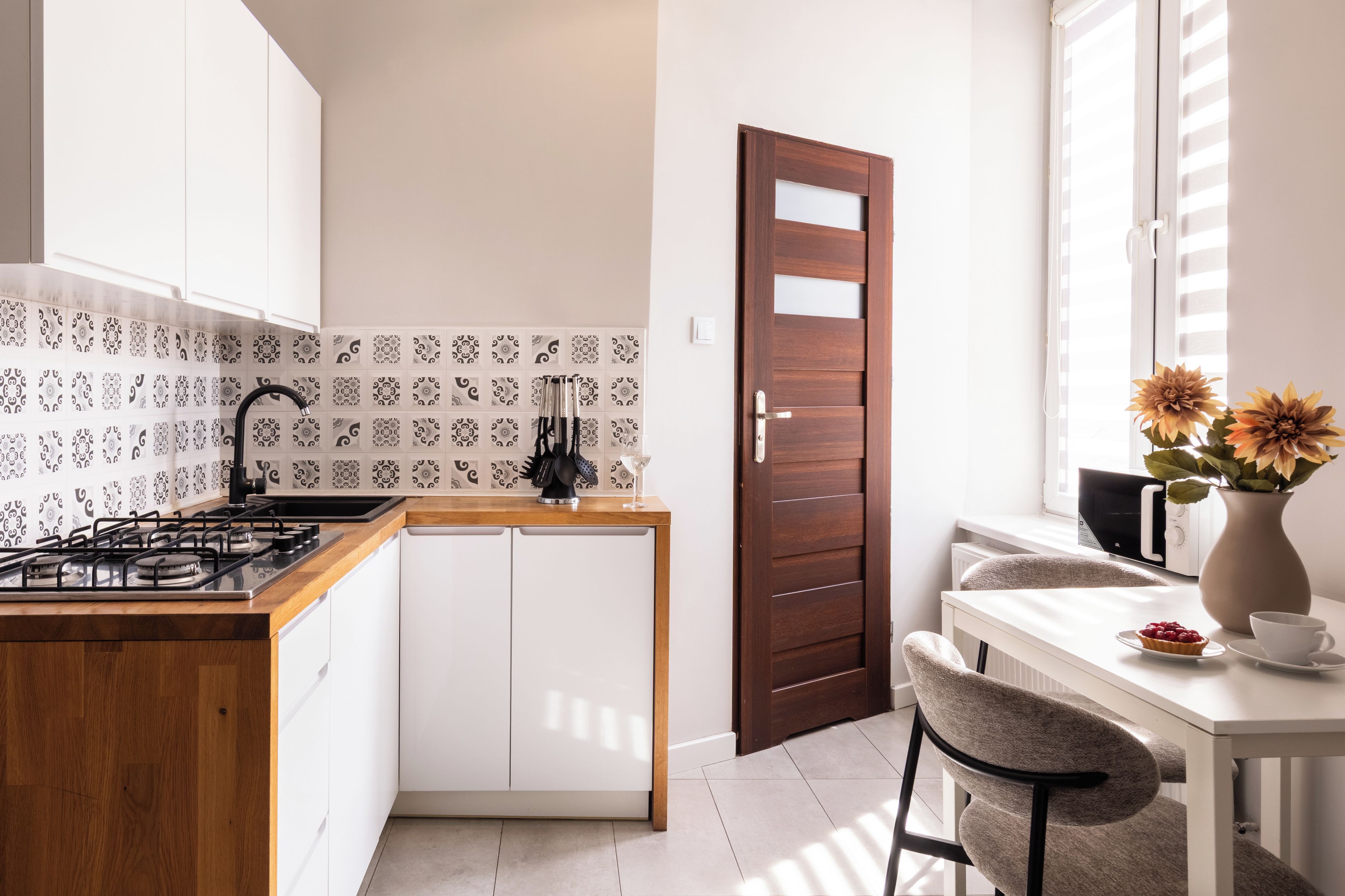 A modern kitchen with a gas stove, white cabinets, patterned backsplash, and a wooden door.