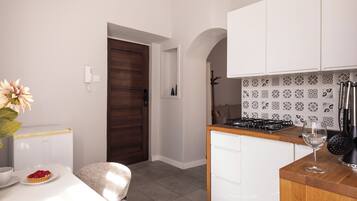 A compact kitchen with a white countertop, a stove, and a sink. There is a door leading to another room and a small table with a plate of food and a glass.