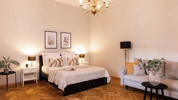 A bedroom with a bed, bedside tables, a nightstand, a sofa, a floor lamp, and a chandelier.