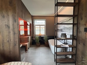 A modern bathroom with a bathtub, wooden shelving, and a view of the outdoors. - Strandhuus, Apartment 2 "strandlaufer" (Grossenbrode)