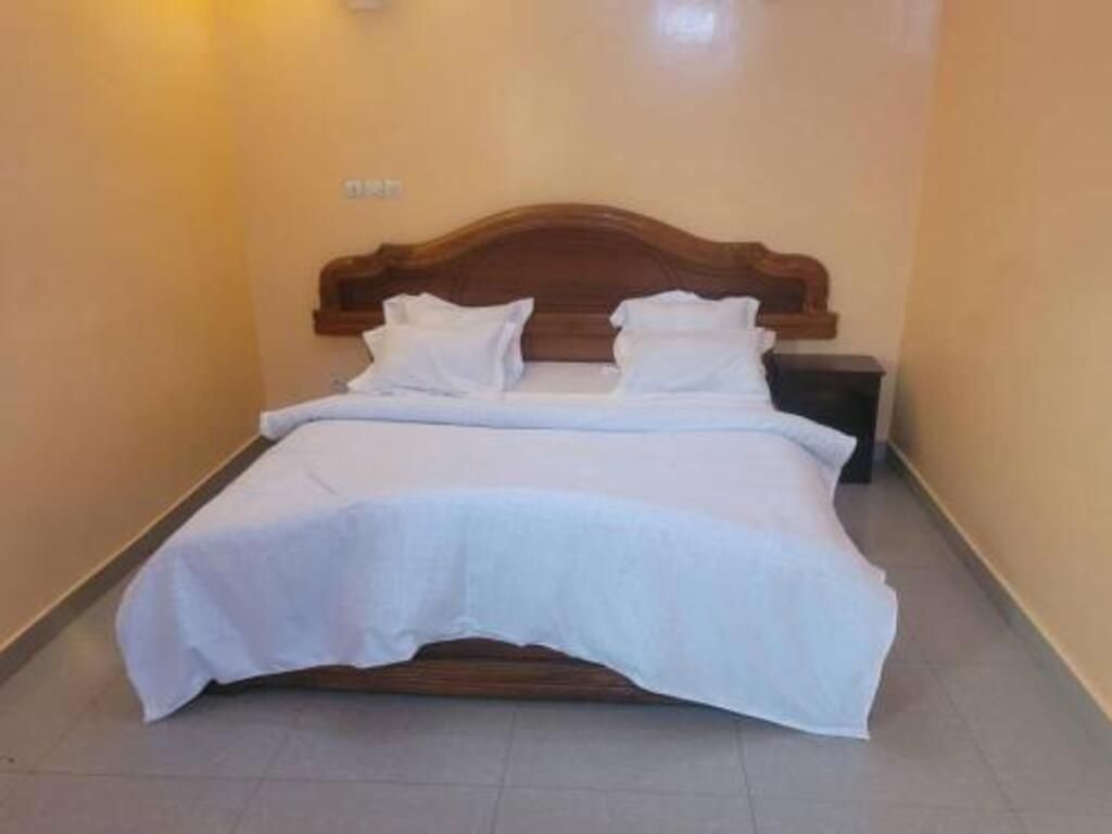 A single bed with a wooden headboard and white bedding in a room with beige walls.