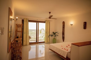 A bedroom with a bed, a wooden chair, a potted plant, a ceiling fan, and a view of the ocean through a sliding door. - Amani Bahari (Marumbi)