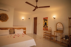 A hotel room with a bed, a ceiling fan, a wooden door, a painting, and a mirror. - Amani Bahari (Marumbi)