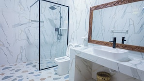 A bathroom with a glass shower enclosure, a white sink, and a marble-patterned wall. - Amani Bahari (Marumbi)