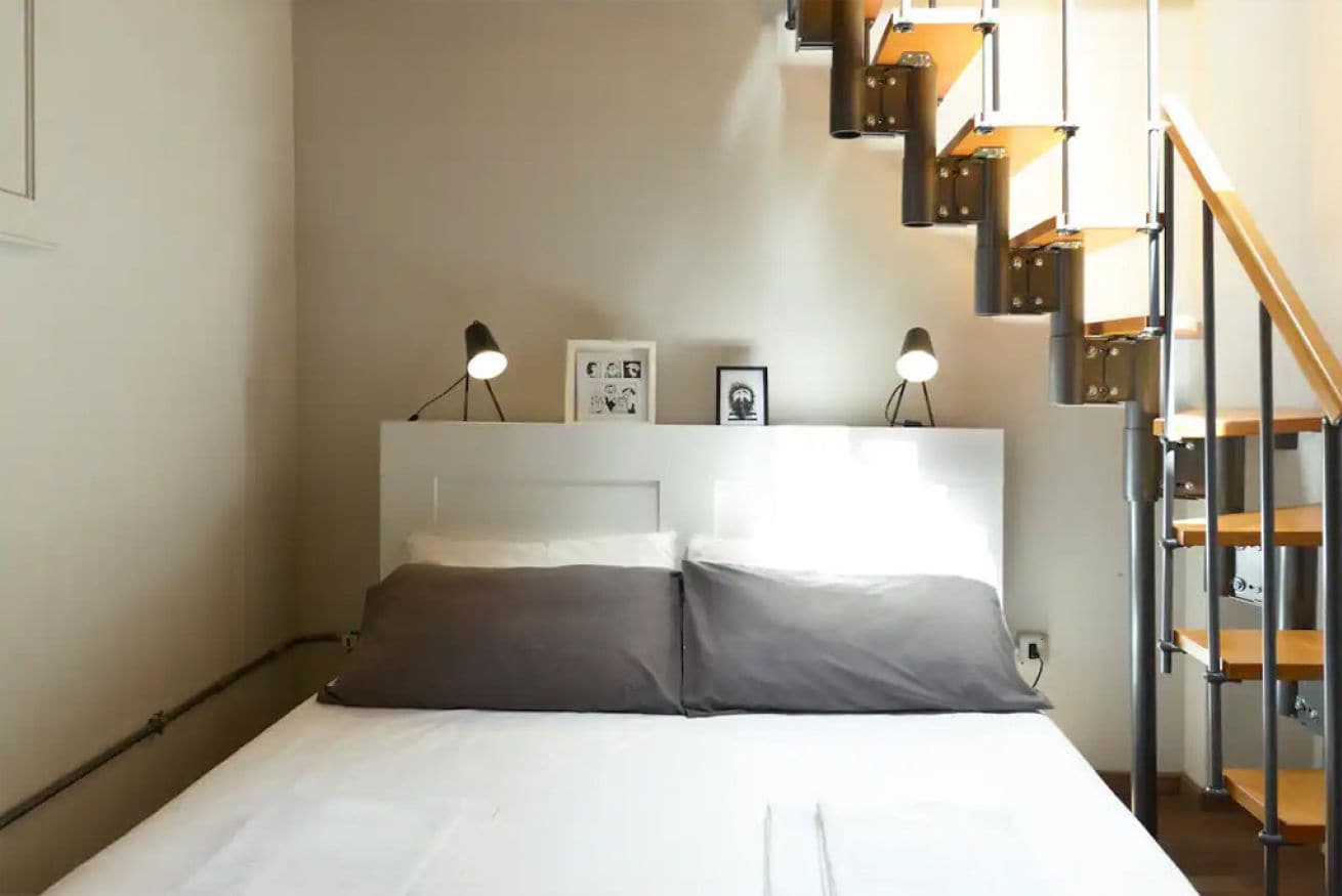 Un dormitorio con cama, dos lámparas de noche, cabecera y una escalera con barandilla.