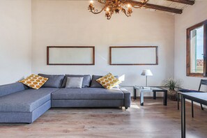 A living room with a sectional sofa, two framed pictures on the wall, a table, a lamp, and a potted plant. - Otomo Flat-Steps from SMN Station&Airport tram (Florence)