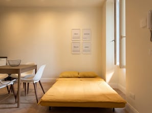 Ein kleiner, moderner Raum mit einem Bett, einem Schreibtisch und zwei Stühlen. An der Wand befinden sich gerahmte Texte.