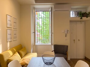 Ein Zimmer mit Fenster, einer Couch, einem Sessel, einem Tisch und einer Tür.